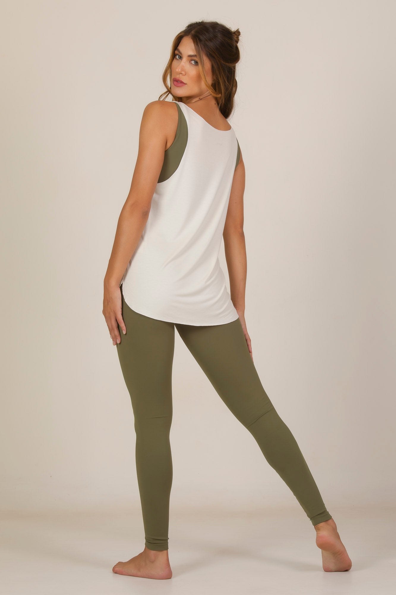 Model showcasing the Over Tank Top in white, paired with olive green leggings, highlighting its sporty and oversized style.